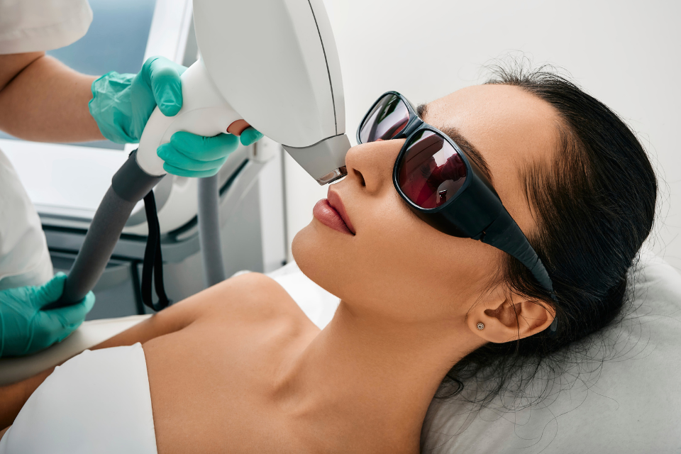 A patient wearing protective laser safety glasses receives a physician-guided laser treatment on her face from a medical professional.